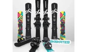 Narty do skakania i snowboardy z kolorowymi grafikami. Dwa zestawy nart do skakania z czarnymi wiązaniami i grafiką górską. Dwa snowboardy z kolorowymi wzorami.