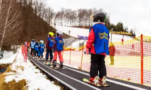 Dzieci na taśmie narciarskiej, idealnej dla początkujących narciarzy. W tle las i stoki.