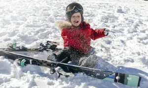 Mały narciarz w czerwonej kurtce, z goglami na głowie, siedzi w śniegu obok nart. To jego pierwsze narty dla dzieci 4 lata, ale zabawa jest przednia!