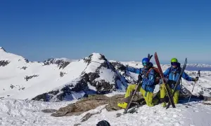 Dwóch narciarzy w kaskach i goglach na szczycie ośnieżonej góry, gotowych do zjazdu. To ich skipass do wolności!