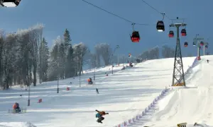 Kolejka gondolowa nad ośnieżonym stokiem narciarskim, na którym snowboardzista wykonuje skok.
