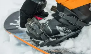 Rękawica zapina but snowboardowy na desce, przygotowując się do wygrzewania butów snowboardowych w śniegu.
