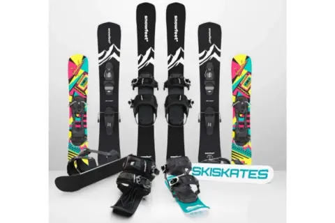 Narty do skakania i snowboardy z kolorowymi grafikami. Dwa zestawy nart do skakania z czarnymi wiązaniami i grafiką górską. Dwa snowboardy z kolorowymi wzorami.