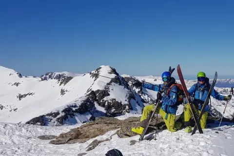 Dwóch narciarzy w kaskach i goglach na szczycie ośnieżonej góry, gotowych do zjazdu. To ich skipass do wolności!