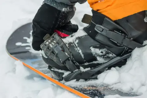 Rękawica zapina but snowboardowy na desce, przygotowując się do wygrzewania butów snowboardowych w śniegu.