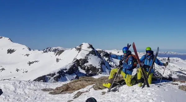 Dwóch narciarzy w kaskach i goglach na szczycie ośnieżonej góry, gotowych do zjazdu. To ich skipass do wolności!