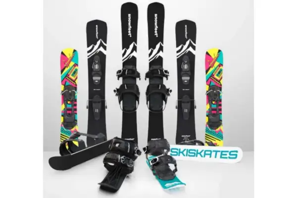 Narty do skakania i snowboardy z kolorowymi grafikami. Dwa zestawy nart do skakania z czarnymi wiązaniami i grafiką górską. Dwa snowboardy z kolorowymi wzorami.